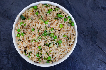 Wild and brown rice pilaf with green peas, onion and baby marrow on black slate with copy space