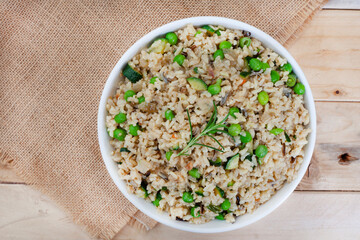 Wild and brown rice pilaf with green peas, onion and baby marrow on rustic wood with burlap and copy space
