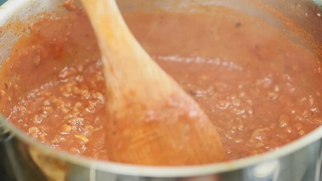 Tomato sauce with mince is boiling and stirring in a pot.
