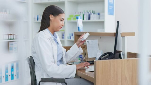 Young pharmacist working on computer at a pharmacy counter. Woman using technology to access drug database, does inventory checkup and dispensing online medicine prescriptions in a drugstore