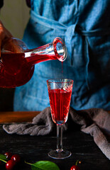 A woman's hand pours cherry liqueur into a glass. Homemade cherry liqueur