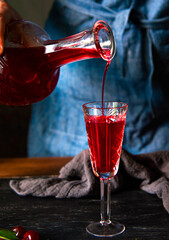 A woman's hand pours cherry liqueur into a glass. Homemade cherry liqueur