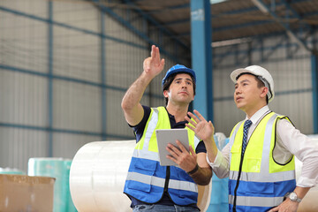 Architect or engineering man and worker sitting and checking large warehouse with computer. Multiethnic two business manager pointing and looking in future with warehouse building background.