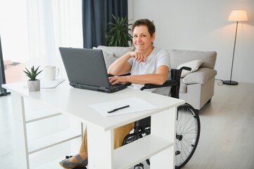 Freelancer in wheelchair using laptop near notebook and papers on table