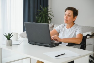 Positive elderly woman in wheelchair working on laptop, IT freelancer, online