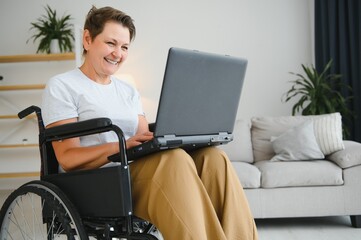 Middle age woman using laptop sitting on wheelchair at home