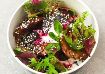 Salad of lettuce, beet and chicken liver with fresh radicchio and sesame seeds in a takeaway round container topped with yoghurt sauce on gray background. Healthy food delivery concept.