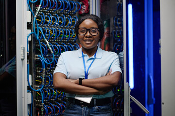 Portrait of African female engineer smiling at camera standing with her arms crossed in data server...