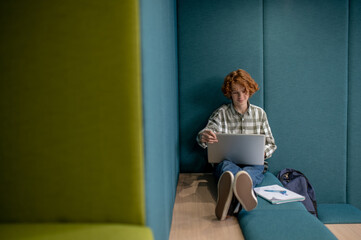 Ginger boy sitting with a laptop and watching something online