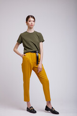 Fashion photo of a beautiful elegant young asian woman in a pretty yellow pants, green t-shirt, belt posing over white, soft gray background. Studio Shot.