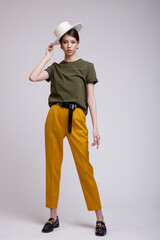 Fashion photo of a beautiful elegant young asian woman in a pretty yellow pants, green t-shirt, belt, hat posing over white, soft gray background. Studio Shot.