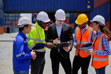 Group of multiracial workers in safety uniforms and hardhats work at logistics terminal dock with stacks of containers, loading control, and management shipping goods, cargo transportation industry.