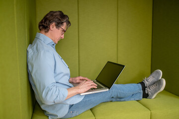 A man in eyewear sitting with a laptop in a lounge zone