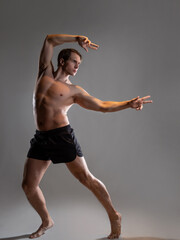 Muscular man in an artistic pose, portrait on a gray background. An athlete guy with spectacular muscles poses like an antique hero