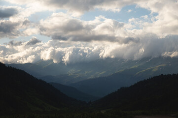 Mountain forest gorge landscape, clouds cling to the tops of high mountains, a glimpse of the sun's rays