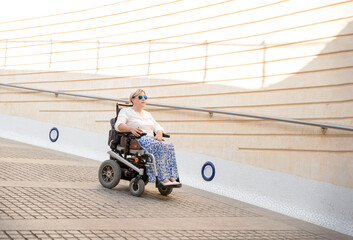 a woman with sunglasses sitting in an electric wheelchair going down an urban ramp. Concept of a...