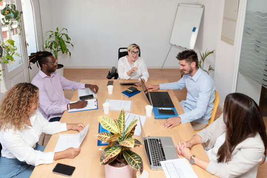 Top View Of Group Of Multiethnic Busy People Working In An Office, A Woman The Team Leader In The Wheelchair Explaining Business Strategy. Business Meeting Concept