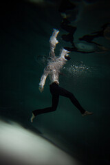 Beautiful underwater shooting, guy in white shirt and pants has fallen under the water and is drowning. a young man relaxes down under surface of the water, waves and refraction of light under water