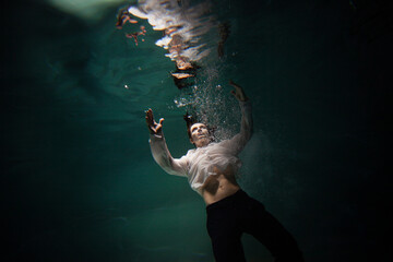 underwater shooting with contrasting light, a guy is swimming underwater, pulling his hand to his...