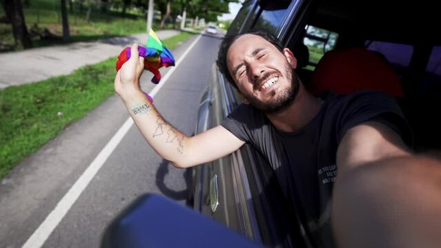 Slow motion of caucasian male gay celebrating lgtb lesbian pride flying rainbow flag outside window car while drive fast on the highway