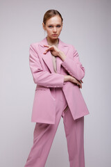 Fashion photo of a beautiful elegant young woman in a pretty soft pink oversized suit, jacket, pants, sneakers posing over white, soft gray background. Studio Shot.
