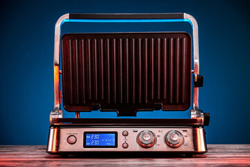 open electric grill stands on a wooden table on a blue background