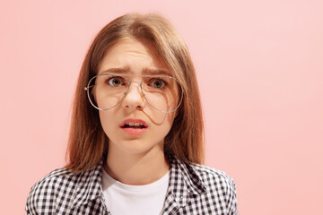 Portrait of young emotive girl in glasses posing with shocked expression isolated over pink studio...