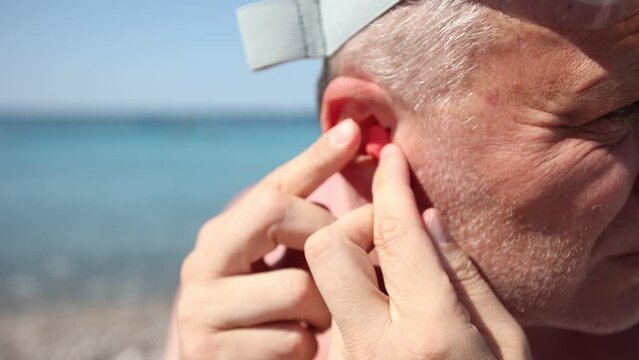Mature man putting silicone ear plugs, surfers earplugs, swim plugs