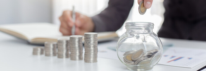 Businessmen put coins in a piggy bank and record income - income tax expenses in the office, Financial accounting and save money concept.
