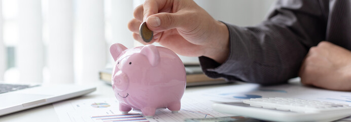 Businessmen put coins in a piggy bank and record income - income tax expenses in the office,...