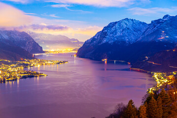 Panorama showing the Lecco shore of Lake Como, on a winter evening, with clouds and snow capped...