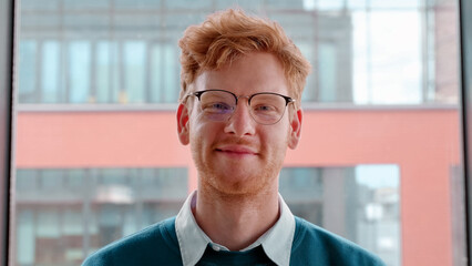 Young ginger irish man in glasses smiling with pleased happy expression and looking at camera portrait. Millennial male freelancer successful entrepreneur,young businessman standing in office. Slow mo - obrazy, fototapety, plakaty
