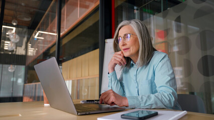  Senior businesswoman sitting at working place and looking at camera