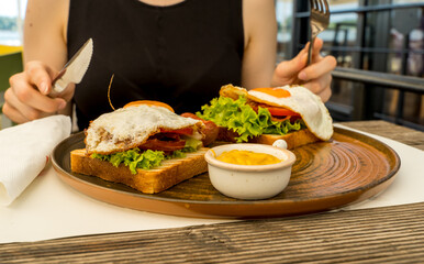 A close up girl is eating healthy English breakfast during the day in a restaurant cutting sausage and sandwich 