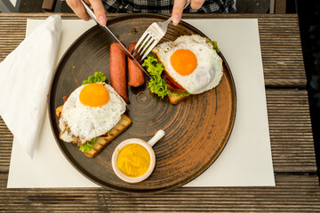 A close up girl is eating healthy English breakfast during the day in a restaurant cutting sausage and sandwich 