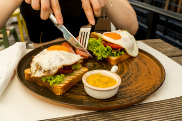 A close up girl is eating healthy English breakfast during the day in a restaurant cutting sausage and sandwich 