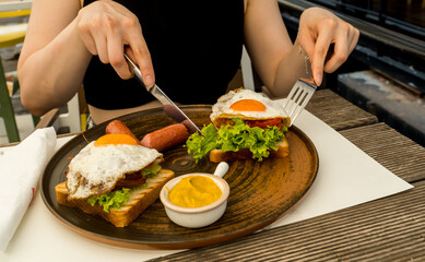 A close up girl is eating healthy English breakfast during the day in a restaurant cutting sausage and sandwich 
