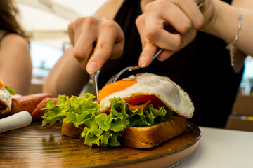 A close up girl is eating healthy English breakfast during the day in a restaurant cutting sausage and sandwich 