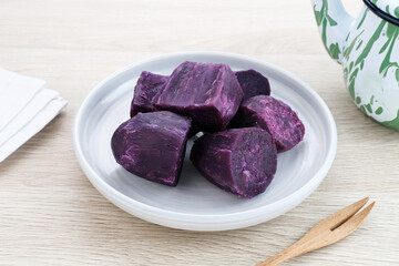 Steamed Purple Sweet Potato (Ubi ungu kukus) served in white plate on wooden table. 
