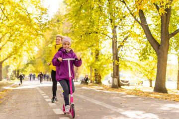 Little girl learns to ride a scooter in a park in autumn