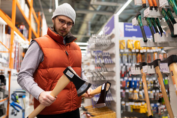 a man in a construction hypermarket chooses a household ax