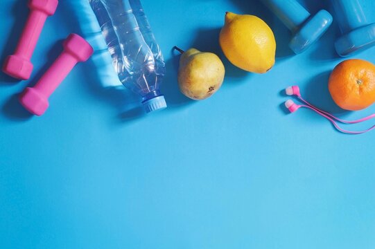 Fitness equipment on a blue background flat lay photo. Dumbbells, mineral water, fruits and headphones. Gym, fitness, healthy lifestyle concept