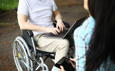 Fototapeta na wymiar Man in wheelchair and woman work remotely while sitting in park