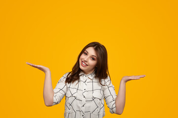 Positive young lady shrugging shoulders against yellow background