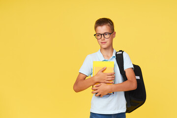 Portrait of a schoolboy in glasses with textbooks and a backpack on a yellow background. Back to...
