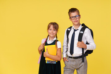 Portrait of a school girl and boy with textbooks and a backpack on a yellow background. Back to...