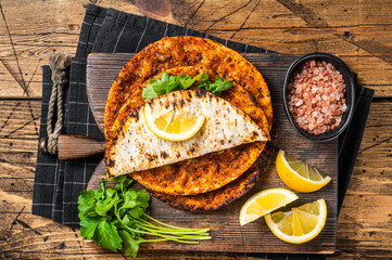 Turkish cuisine made with thin dough and minced beef meat lahmacun on wooden board with herbs. Wooden background. Top view