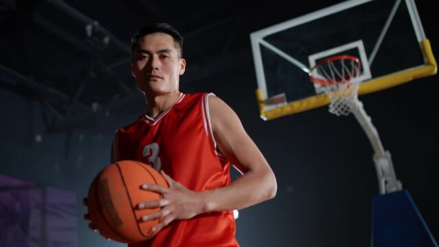 Portrait of an asian basketball player, holding a ball in her hands and serious looking at the camera, international basketball championship.
