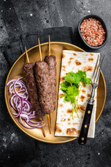 Lamb meat kofta kebab, onion and flat bread on plate. Black background. Top view