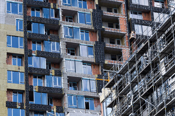 Obraz premium Construction work is underway in a new residential multi-storey brick and concrete block apartment building, around which scaffolding has been installed to provide access for outdoor work